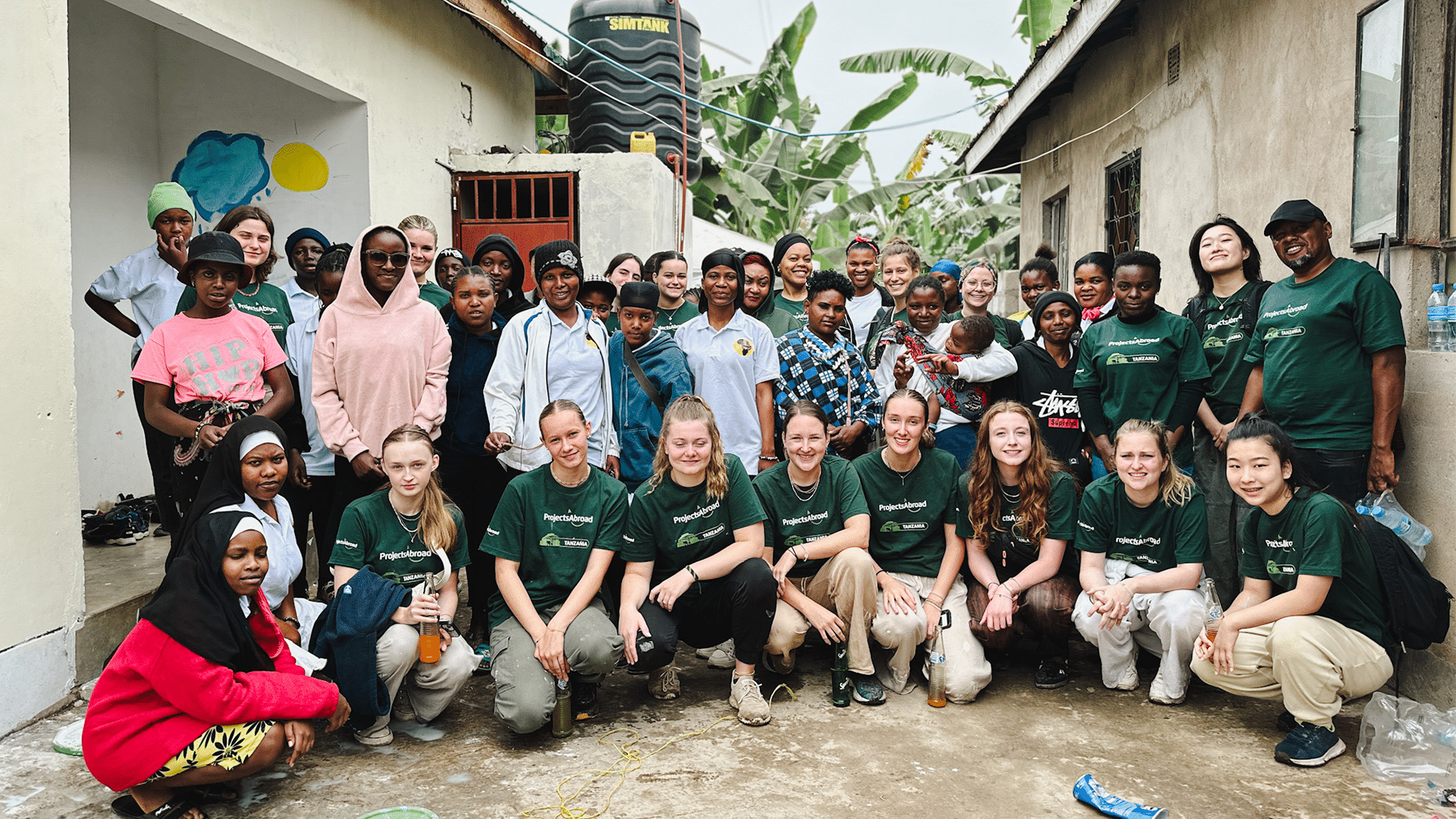 A large group of Projects Abroad volunteers and local community members posing for a group photo outside a building in Tanzania.